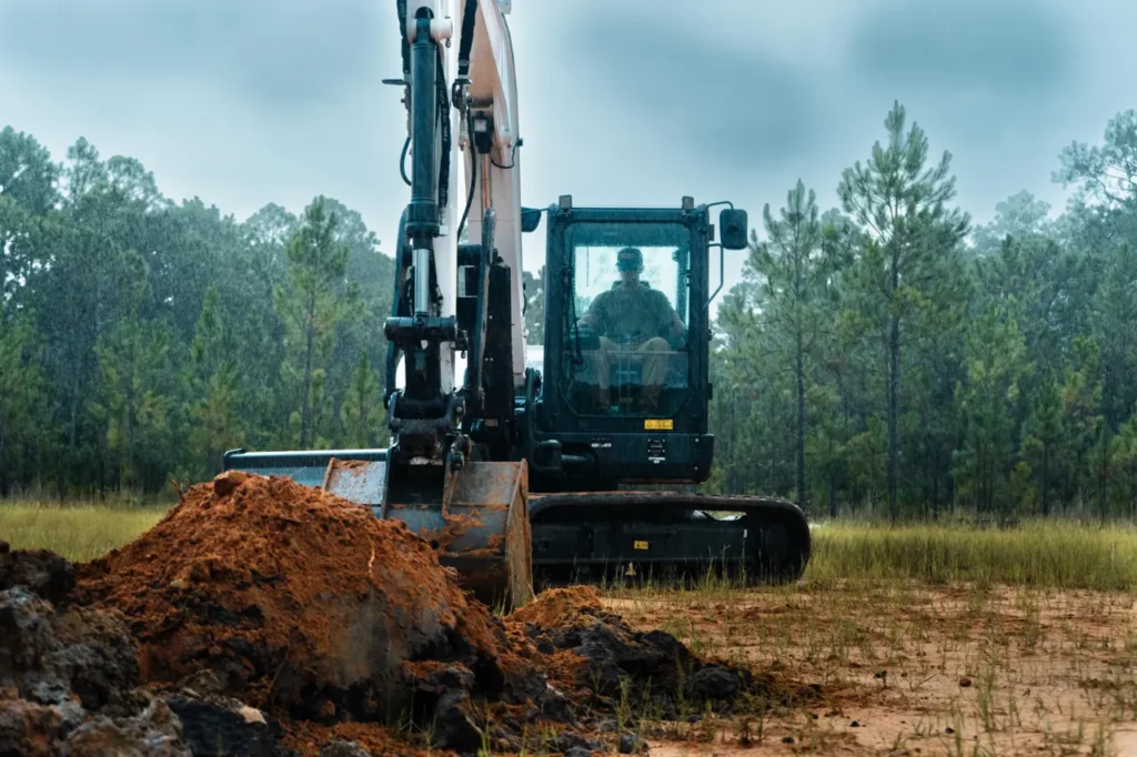 Bobcat E88 excavator digging in an open field with pines behind