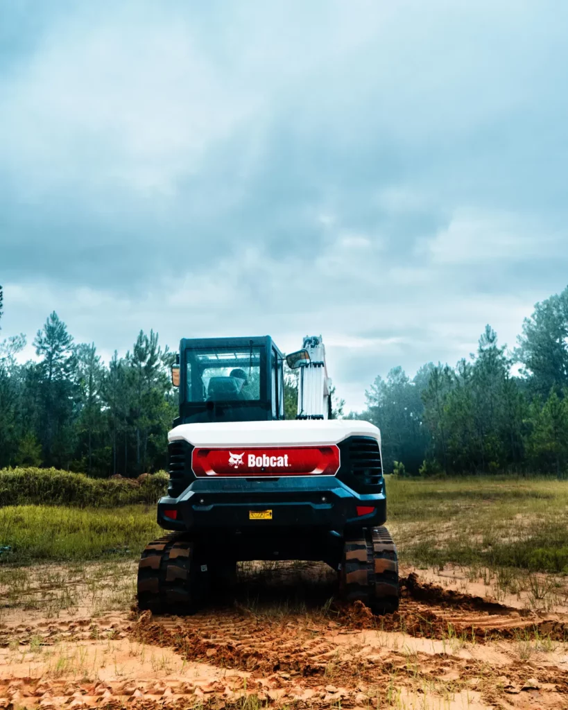Bobcat E88 excavator on graded ground at the edge of a pine stand