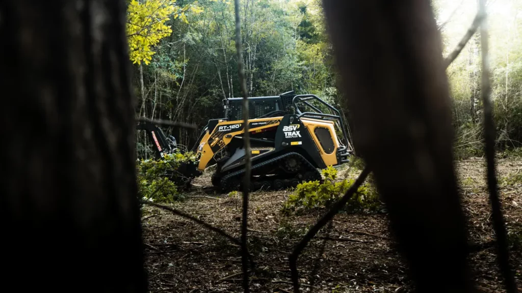 ASV RT-120 forestry mulcher working a cleared patch of woods, framed between two pine trunks